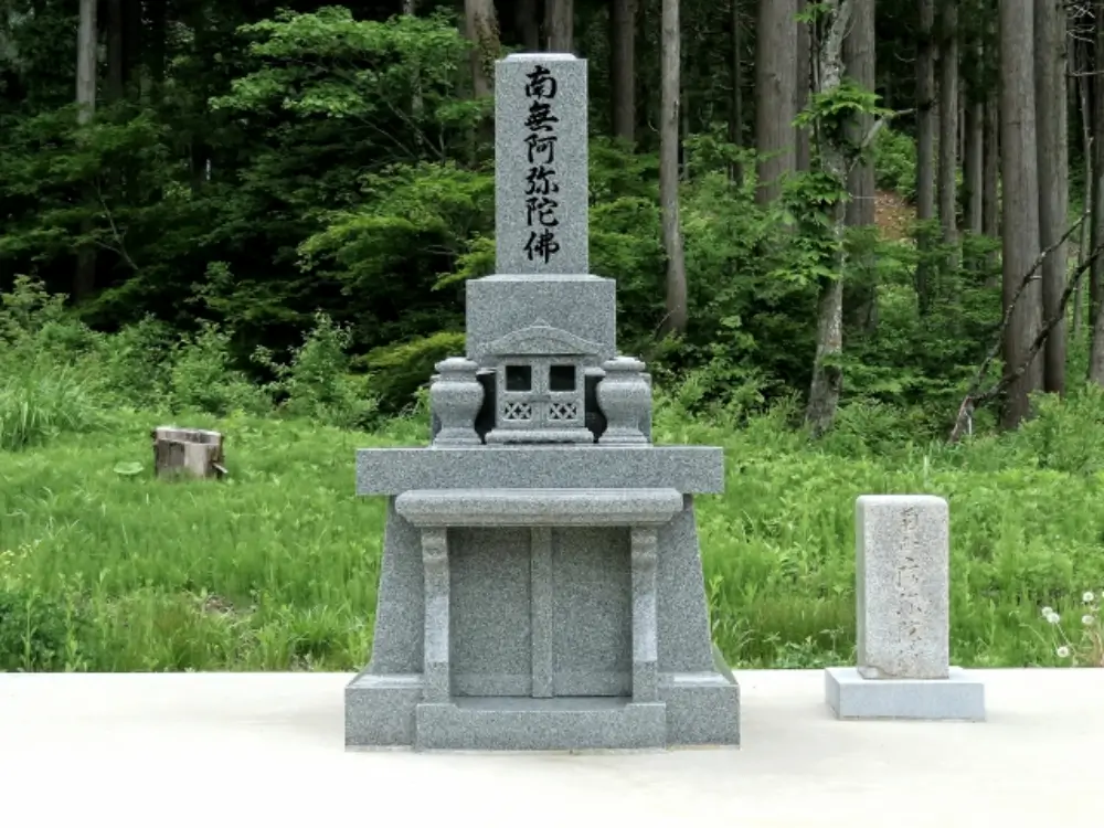 緑の自然に囲まれた場所に建つ「南無阿弥陀仏」と彫られた墓石塔の写真