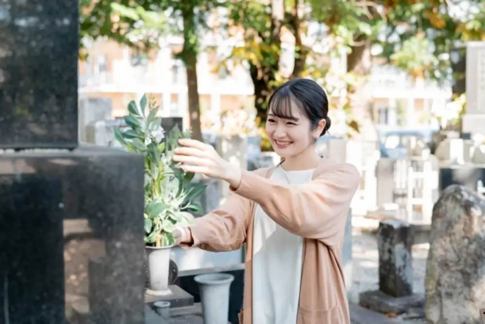 　若い女性がお墓に花を供えている笑顔の様子