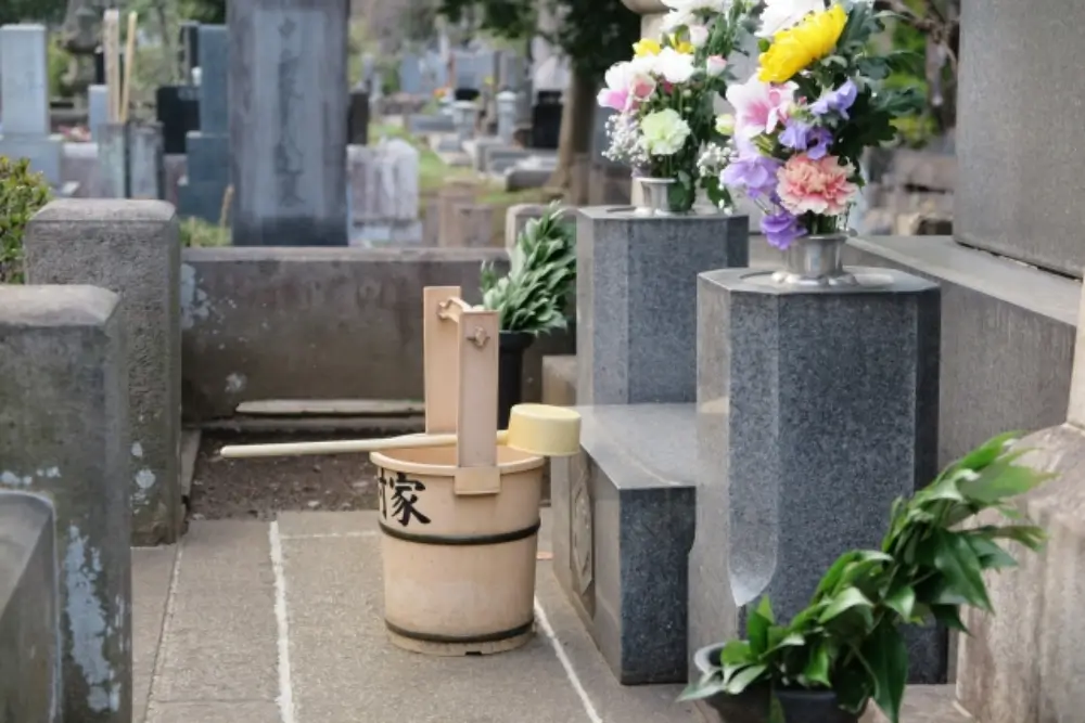 お墓の前に供えられた花と、墓参り用の桶と柄杓が置かれている様子