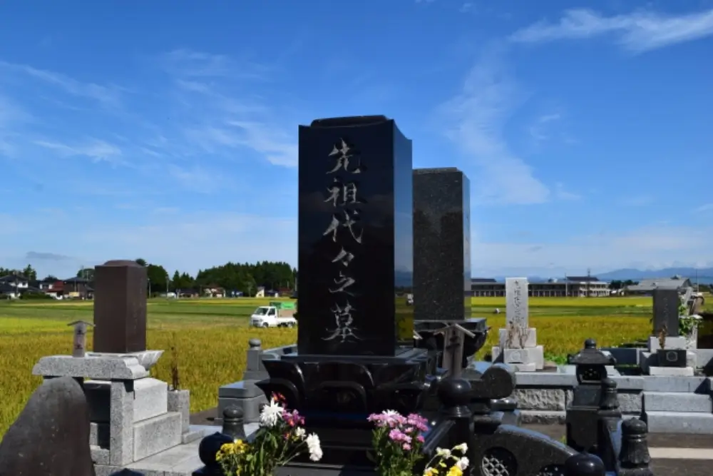 田園風景の中に建てられた黒御影石の墓石と花