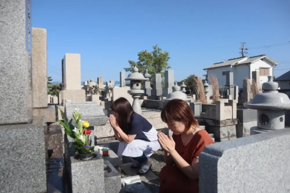 墓前で手を合わせて祈る二人の女性の様子