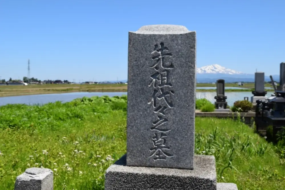「先祖代々之墓」と刻まれた墓石と田園風景、遠くに雪山が見える風景