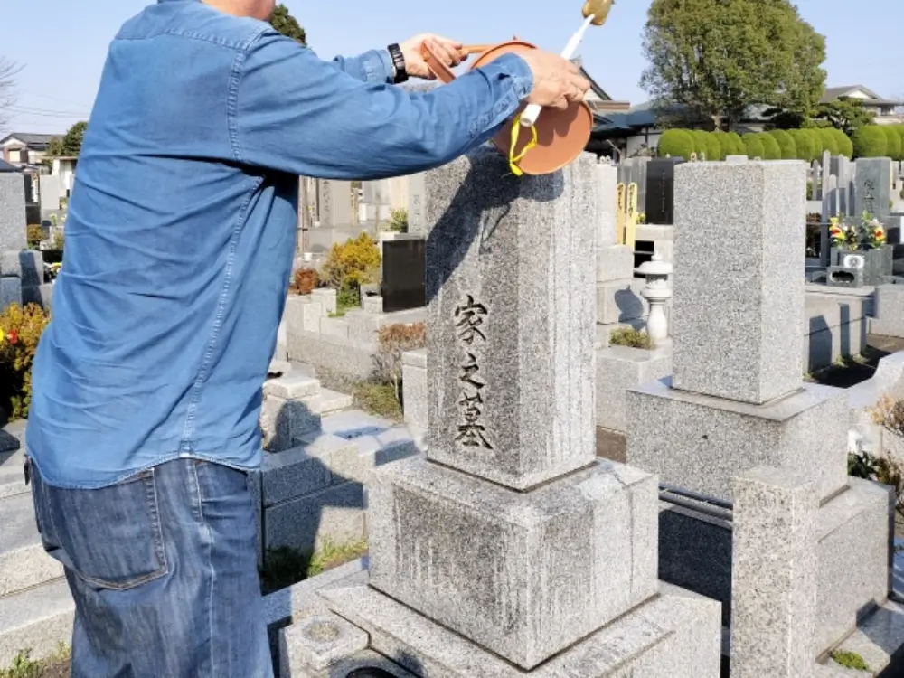 家之墓と刻まれた墓石を水で清掃する男性の後ろ姿