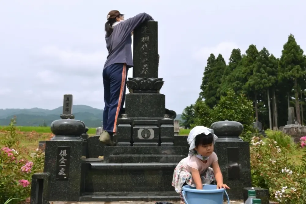 子どもが一緒にお墓を掃除している微笑ましい場面 母は墓石を掃除している様子