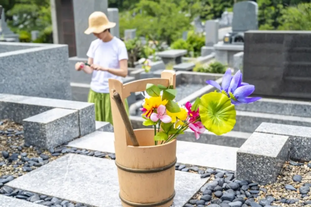 お墓参り用の桶と花と女性が線香を持っている様子