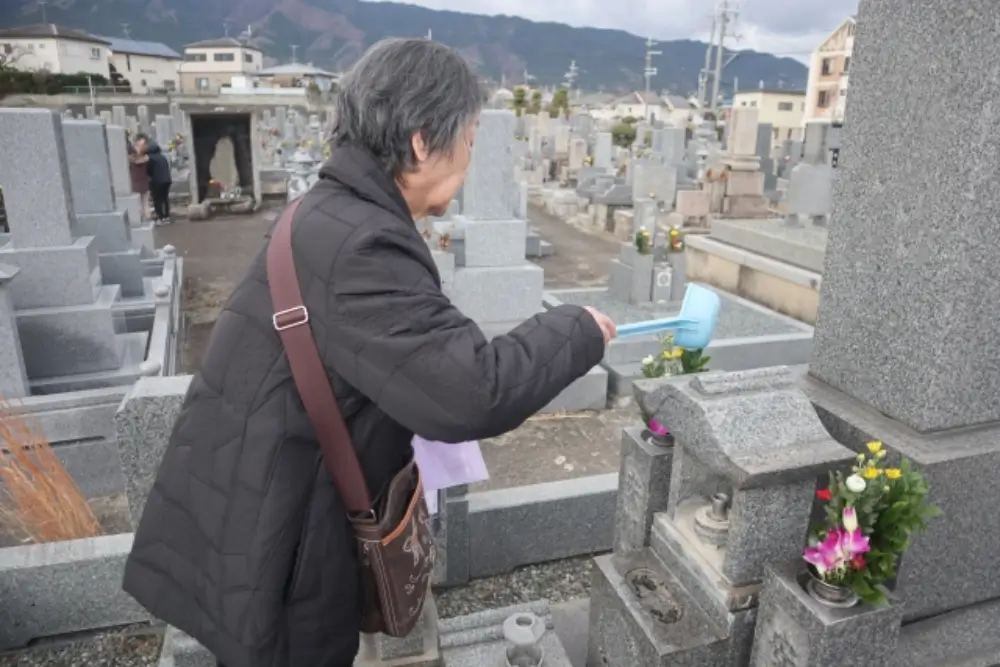 お墓に水をかけて掃除する高齢女性の姿