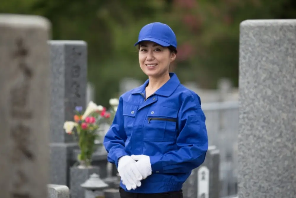お墓に供えた花の前で微笑む女性清掃員
