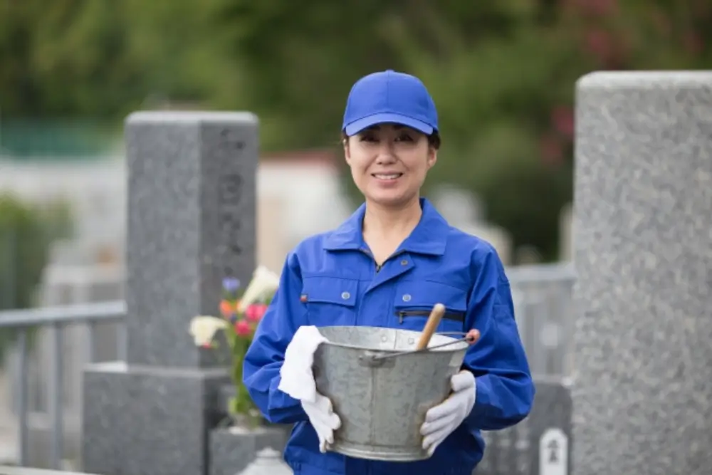 墓地でバケツを持つ女性清掃スタッフ