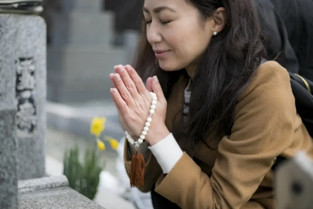 お墓の前で数珠を持って手を合わせる女性の様子