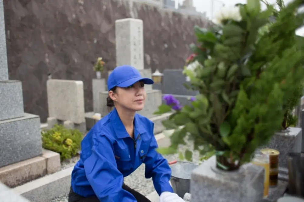 墓前で清掃をする青い作業着の女性(正面から)