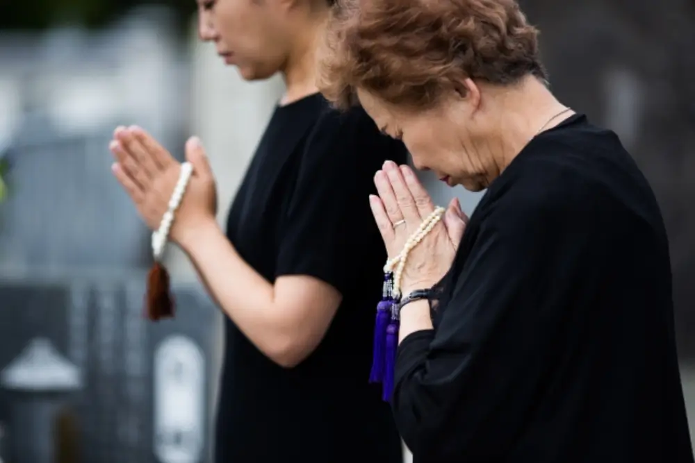 お墓の前で手を合わせて祈る高齢女性の姿