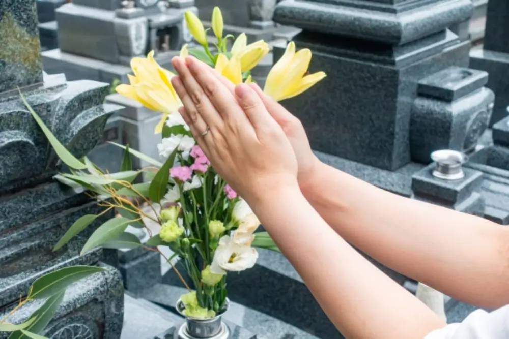 墓前の花に手を合わせて祈る人の手元の様子