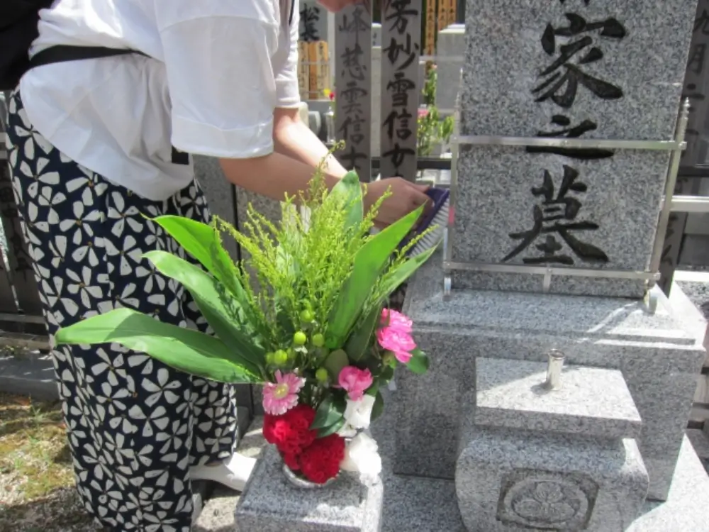 「家之墓」と刻まれた墓石に赤やピンクの花を供えている人の姿