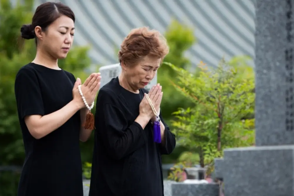 黙祷を捧げる年配女性とその娘のお墓参りの光景