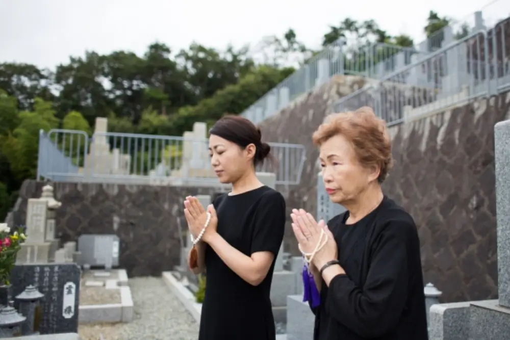 墓前で手を合わせて祈る母娘の姿