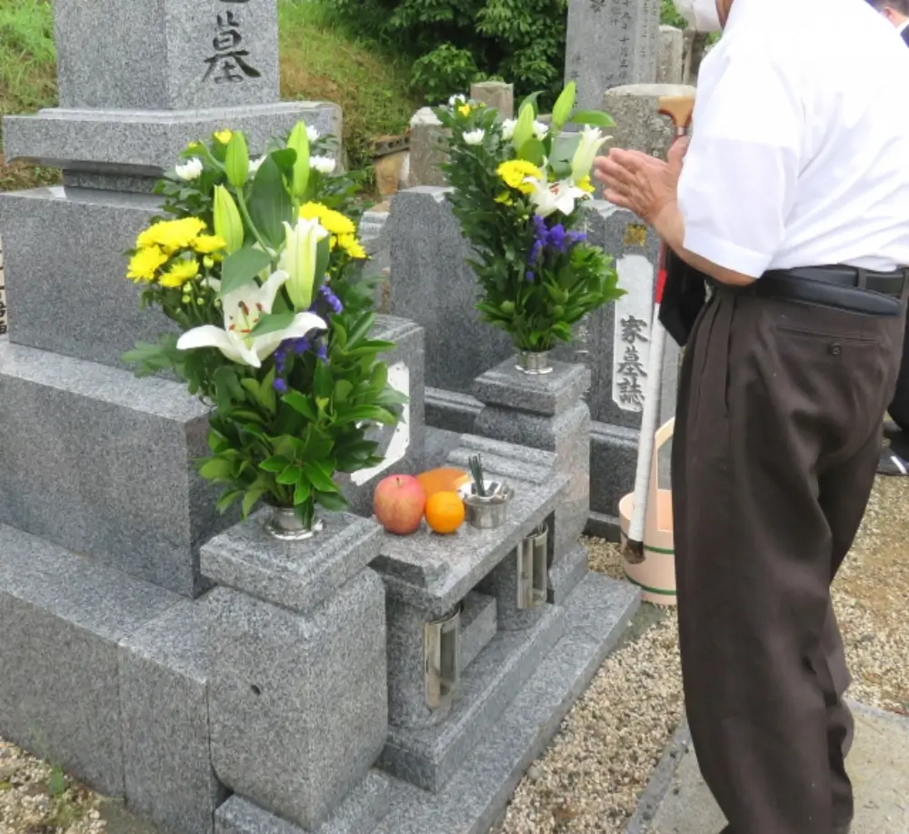 墓前に花と果物を供え、手を合わせる男性の姿