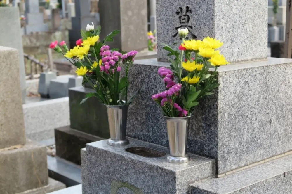 墓石の前に黄色と紫の菊の花が左右に供えられている様子