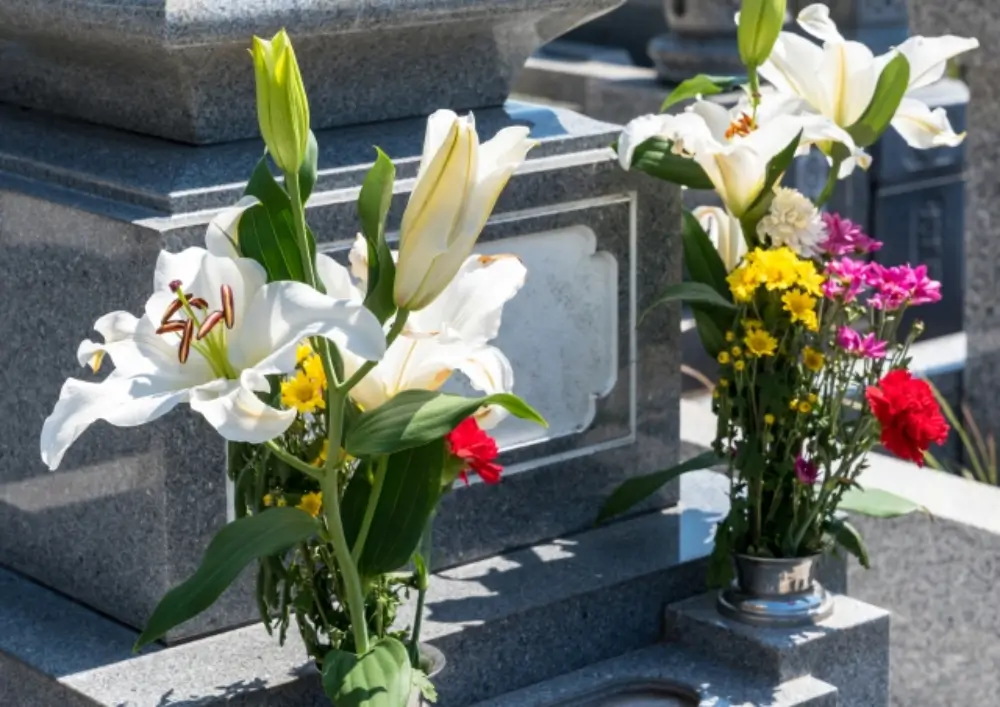 白いユリと黄色・赤・ピンクの菊が花立に供えられている墓前の様子