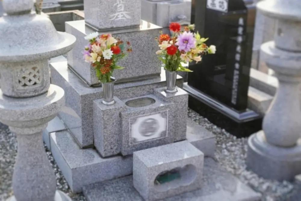 明るい色の墓石の前に、赤やピンクの生花が供えられた2つの花立が並んでいる様子