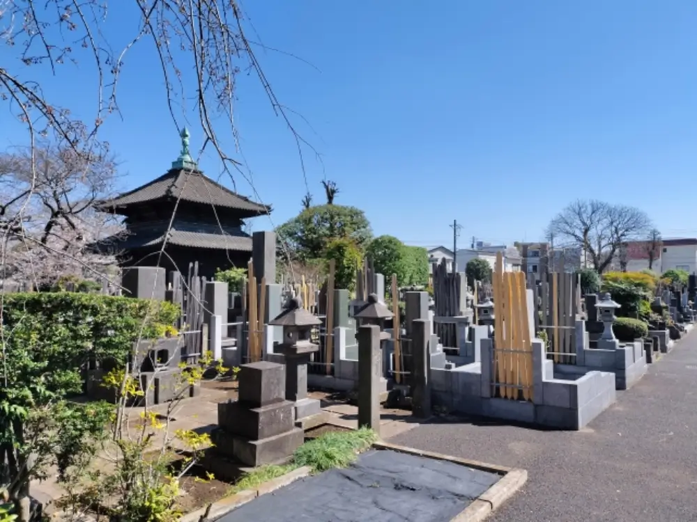 青空の下、お寺と整然と並ぶ墓地が見える風景。供養や法要の季節感も漂う