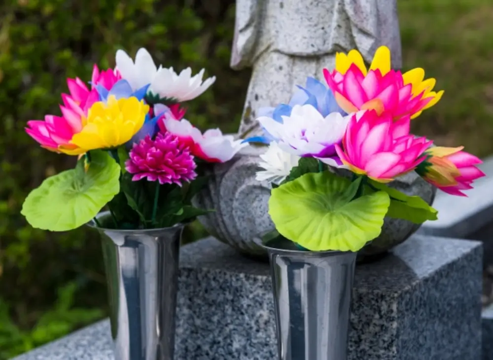 石仏の前にカラフルな蓮の造花が花立に供えられている墓前の写真