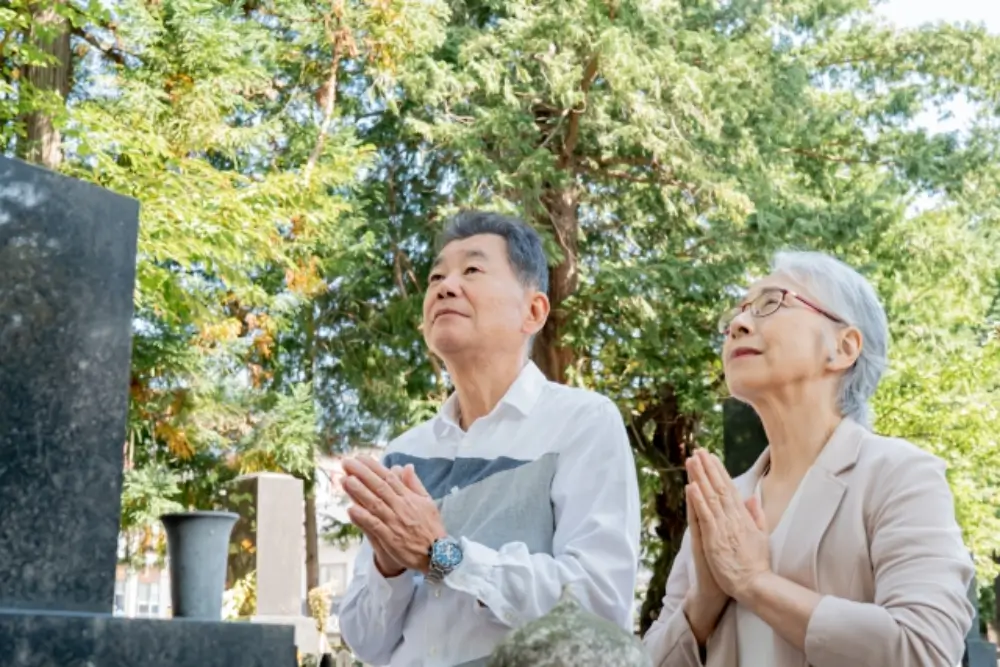 高齢の夫婦がお墓の前で手を合わせている様子