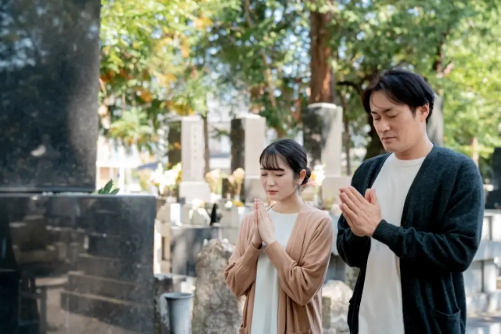若い夫婦が墓前で手を合わせてお参りしている様子