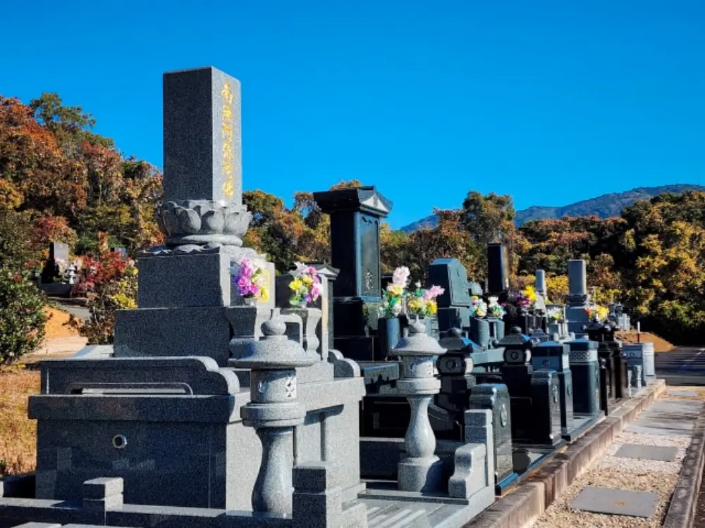 青空の下、供花が飾られた墓石が並ぶ墓地の風景