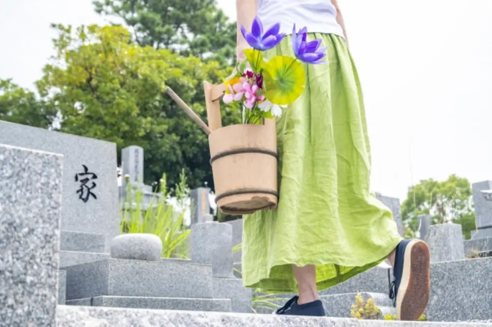 花と柄杓の入った桶を持ち墓地を歩く女性