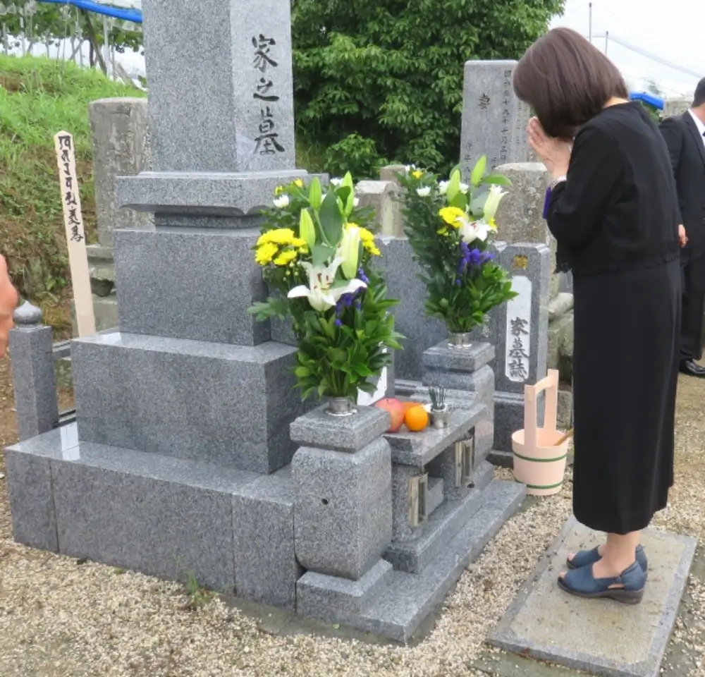 「家之墓」の墓石に手を合わせる女性と供えられた花や果物